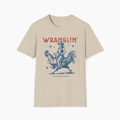Beige t-shirt with a graphic of a cowboy riding a rooster and the word 'WRANGLIN'' on a white background.